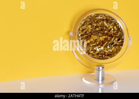 Nahaufnahme eines transparenten runden Kosmetikspiegels mit selektivem Fokus auf die Mitte der vergrößerten Reflexion eines goldenen metallischen funkelnden Farnells OV Stockfoto