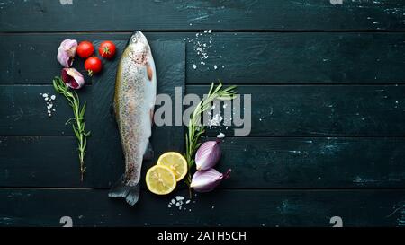 Roher Fisch mit Gemüse auf schwarzem Holzhintergrund. Fischforelle. Draufsicht. Freier Speicherplatz für Ihren Text. Stockfoto