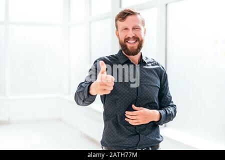 Ein glücklicher Geschäftsmann, der im Büro steht und den Daumen nach oben zeigt Stockfoto