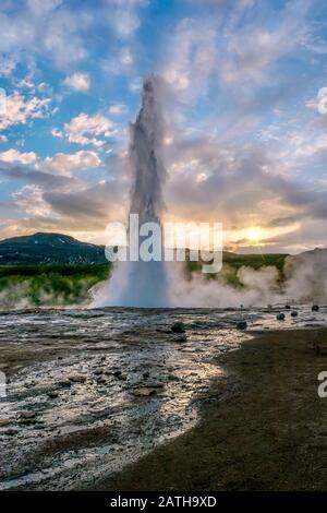 Ein vertikaler Schuss von Strokkur Geysir, einer berühmten heißen Quelle im Südwesten Islands, bricht während eines Sonnenuntergangs im Frühsommer aus. Stockfoto