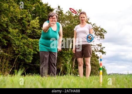 Geistig behinderte Frauen spielen ein Spiel, um ihre motorischen Fähigkeiten, Übungen mit einem Freund oder Therapeuten im Freien auf einer Wiese zu trainieren Stockfoto