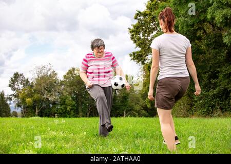 Psychisch behinderte Frauen spielen Fußball, um ihre motorischen Fähigkeiten zu trainieren, Übungen mit einem Freund oder Therapeuten draußen auf einer Wiese Stockfoto