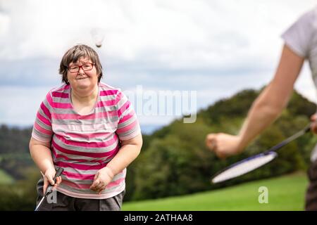 Mentalbehinderte Frau spielt Badminton, um ihre motorischen Fähigkeiten, Übungen mit einem Freund oder Therapeuten im Freien auf einer Wiese zu trainieren Stockfoto