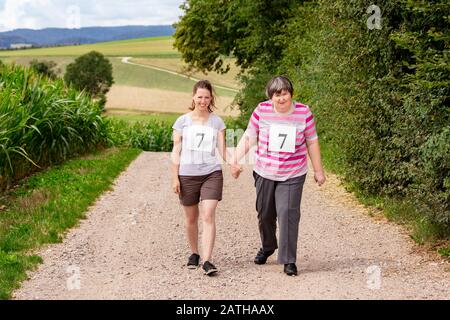 Geistig behinderte Frauen und eine Freundin oder Therapeutin gehen Hand in Hand und tragen Zahlen auf ihrer Oberseite Stockfoto