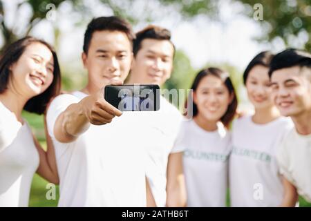 Junge lächelnde Freiwillige fotografieren mit Freunden auf Smartphone, selektive Fokussierung Stockfoto