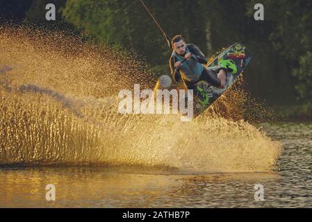 Wakeboarder macht Tricks. Niedriger Winkelschuss des Mannes, der auf einem See weckelt Stockfoto