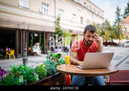 Gestresster, müder junger Mann sitzt vor dem Laptop im Café