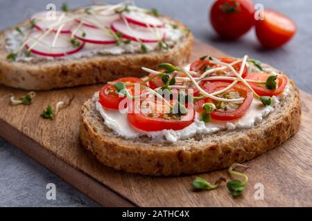 Nahaufnahme eines Sandwiches mit Tomaten, Mikrogrüns und Getreidebrot auf grauem Hintergrund Stockfoto