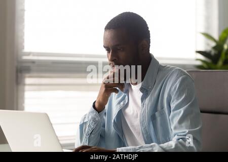 Ein seriöser amerikanischer Mitarbeiter denkt über geschäftliche E-Mails, die auf einem Laptop arbeiten Stockfoto