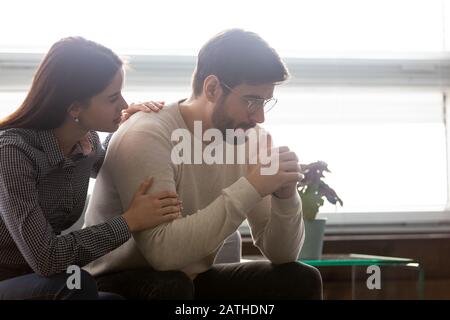 Paare sitzen auf dem Sofa fürsorgliche Frau Umarmungen enttäuschten traurigen frustrierten Ehemann Stockfoto