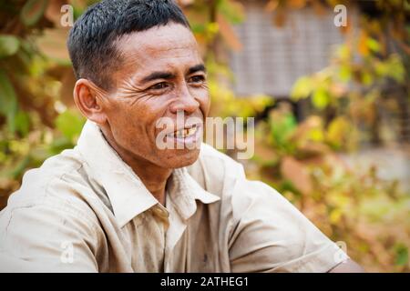 Puok, Provinz Siem Reap, Kambodscha - 4. April 2013: Kambodischer Einheimischer lächelt mit orangefarbenen Blättern Hintergrund Stockfoto