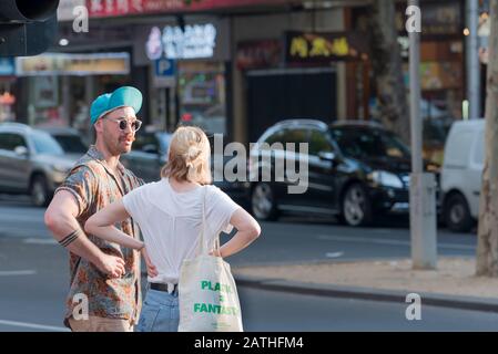 Ein junger Mann in Sonnenbrille und eine hochgedrehte Baseballmütze steht mit einer jungen Frau in einem weißen T-Shirt, an einer Straßenecke im inneren Melbourne, Australien Stockfoto