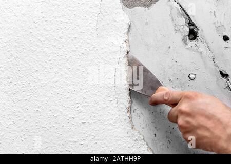 Alte Holzspantapeten werden mit einem Spachtel oder Malerspachtel von der Wand entfernt oder abgeschabt Stockfoto