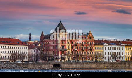 Prag, Tschechien - Panoramablick auf den Prager Fluss im Winter mit traditionellen Gebäuden, Hotels und wunderschönem violettem Himmel bei Sonneneingängen