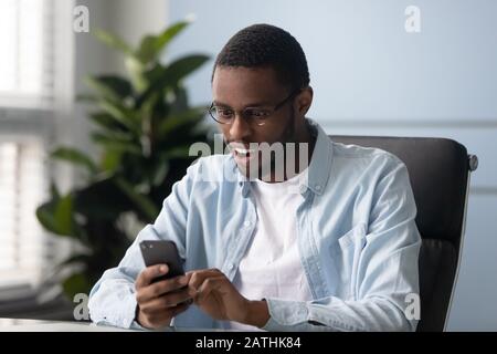 Der afrikanische Ethnicity Guy, der die empfangene Nachricht des Smartphones liest, fühlt sich überrascht Stockfoto