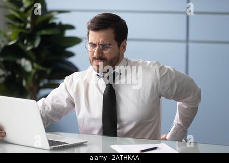 Geschäftsmann reibt sich zurück fühlt sich ungesund, sitzend Arbeitskonzept an Stockfoto