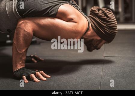Ein bärtiger sportlicher Mann im Fitnessstudio macht Yoga-Übungen. Der Mensch, der die Pose des Yoga Mayurasana macht - Pfauenpose. Stockfoto