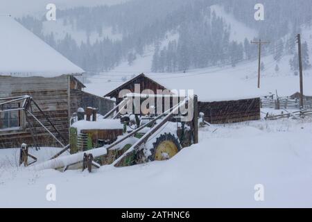 Ein John Deere Heulader-Traktor in einem Schneesturm, an der Seite einer Scheune, in Beavertail, Montana Stockfoto