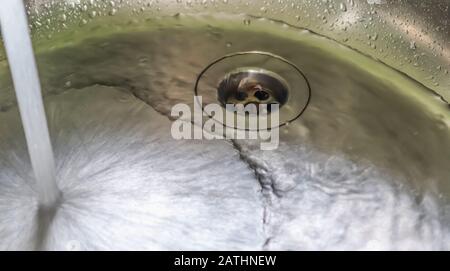 Fließendes Wasser aus einem Wasserhahn in einem metallischen Küchenwaschbecken Stockfoto