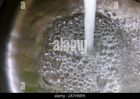 Fließendes Wasser aus einem Wasserhahn in einem metallischen Küchenwaschbecken Stockfoto