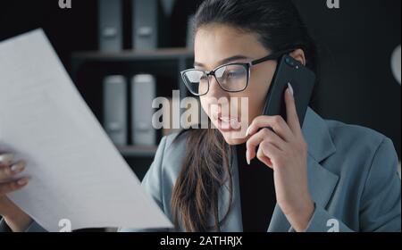Geschäftsfrau, die ein Telefon mit einem Dokument spricht Stockfoto