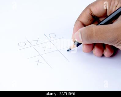 Eine Person, die Tic tac Toe auf einem leeren weißen Papier mit einem schwarzen Holzstift in der Hand spielt Stockfoto