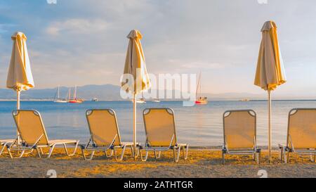 Leere Liegestühle und geschlossene Sonnenschirme an einem sandigen Strand. Reisehintergrund. Start der Saison am Strand. Schöne Landschaft und saisonale Landschaft. Postkarte, Grußkarte, Broschüre. Blick von hinten Stockfoto