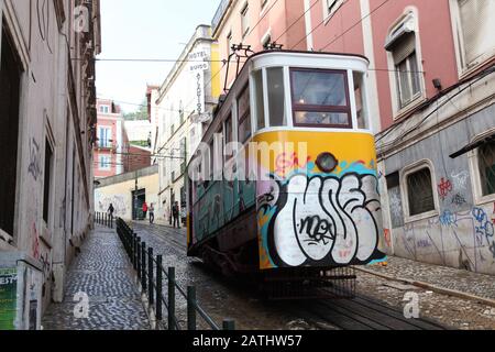 Blick auf eine berühmte Straßenbahn mit bunten Graffiti auf dem Hügel in einer Seitenstraße von Lissabon, Portugal Stockfoto