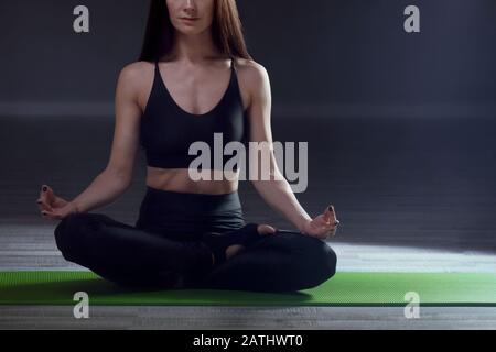 Gesunde junge Frau, die Yoga praktiziert und in Padmasana im Trainingssaal sitzt Stockfoto