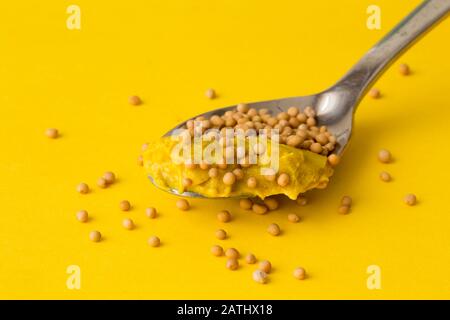 Senfkörner auf Löffel auf hellgelb gefärbtem Hintergrund Stockfoto