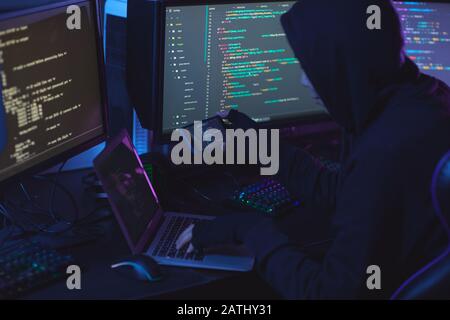Rückansicht bei nicht erkennbarem Cyber-Security-Hacker, der Kapuze trägt, während er an der Programmierung in dunklen Räumen arbeitet, Kopierbereich Stockfoto