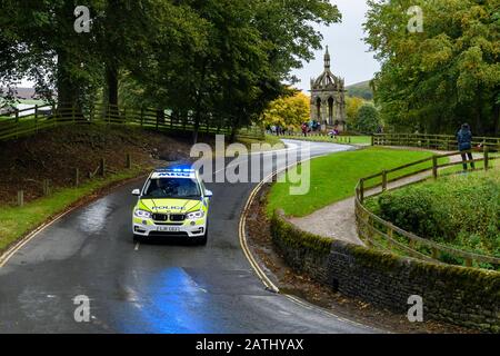 Polizeiwagen, der auf der Landspur mit blinkenden blauen Lichtern fährt und unterwegs ist (BMW-Verkehrskontrollfahrzeug bei der Veranstaltung) - Bolton Abbey, Yorkshire, England Stockfoto