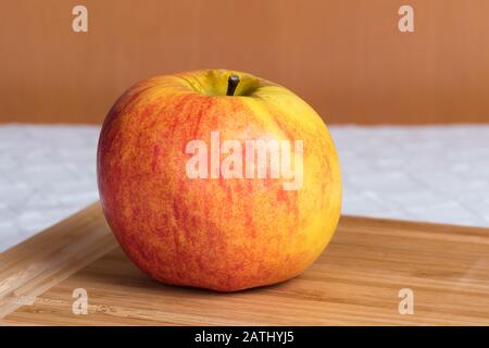 Auf einem Holzbrett auf einem Küchentisch liegt ein reifer apfel (Malus domestica). Stockfoto
