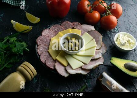 Graue Platte mit Oliven um Salami, Schinken, Käse und Mozzarella. Tomaten, Souce, Oliven, Zitrone, Olivenöl mit Gewürz Stockfoto