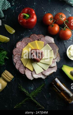 Graue Platte mit Würstchen rund um Salami, Schinken, Käse und Mozzarella. Tomaten, Souce, Oliven, Zitrone, Olivenöl mit Gewürz Stockfoto
