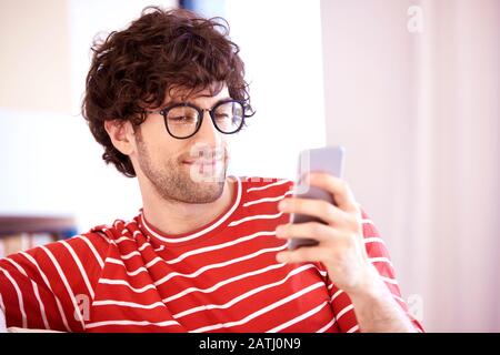 Nahaufnahme der gutaussehenden Textnachrichten junger Mann, während Sie sich zu Hause auf dem Sofa entspannen. Stockfoto