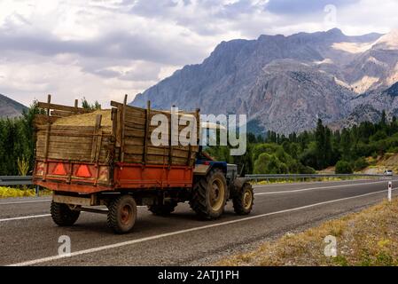 Panoramablick auf die Berge mit Traktor auf der Straße, Wald und bewölktem Himmel im Sommer Stockfoto