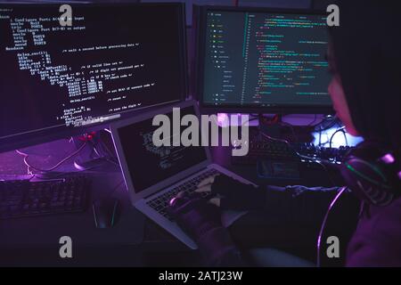 Unerkennbarer junger Mann, umgeben von mehreren Bildschirmen, die Sicherheit im dunklen Raum programmieren oder hacken, Kopierraum Stockfoto