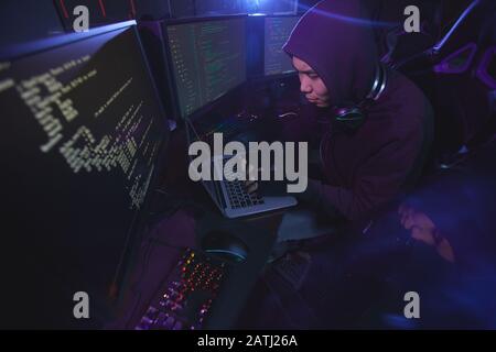 Hochwinkelansicht bei asiatischen Cyber Security Hackern, die Kapuze tragen, während sie an der Programmierung in dunklen Räumen arbeiten, Copy-Space Stockfoto
