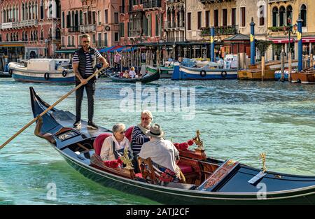 Ein Gondelfahrer lenkt seine Gondel mit drei Touristen, die eine Gondelfahrt entlang des Canal Grande, Venedig, Italien, machen Stockfoto