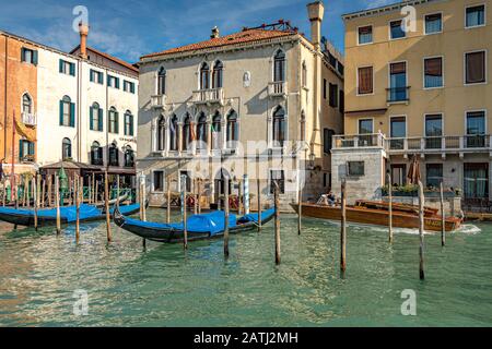 Ein Wassertaxi führt an zwei leeren Gondeln vorbei, die auf Holz-Anlegestellen am Canal Grande, Venedig, aufliegen Stockfoto