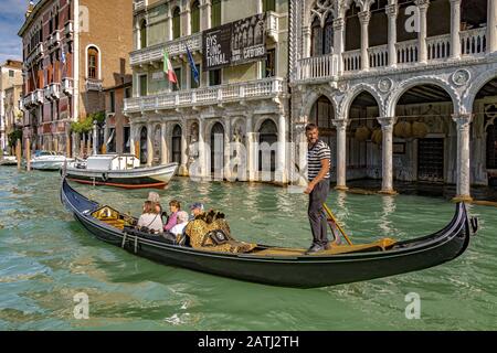 Ein Gondelier, der Touristen für eine Gondelfahrt an der Ca' d'Oro, einem gotischen Palast, entlang Des Canal Grande, Venedig, Italien, vorbeiführt Stockfoto