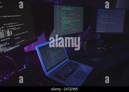 Hochwinkelansicht bei verschiedenen Computergeräten mit Programmiercode auf Bildschirmen auf dem Tisch im Dunkeln Raum, Cyber-Sicherheitskonzept, Kopierraum Stockfoto