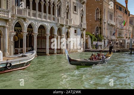 Ein Gondelier, der Touristen für eine Gondelfahrt an der Ca' d'Oro, einem gotischen Palast, entlang Des Canal Grande, Venedig, Italien, vorbeiführt Stockfoto