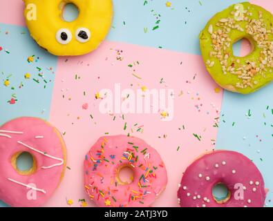 Ganze runde rosa Donuts mit bunten Streuseln liegen auf einer blau-rosa Hintergrund, Ansicht von oben, Pastellfarben Stockfoto