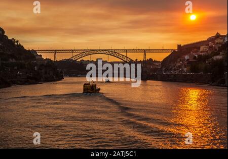 Boote auf dem Fluss Douro bei Sonnenuntergang mit der Brücke Dom Luis I, Oporto, Portugal. Stockfoto