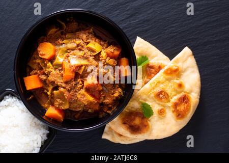 Orientalisches Speisekonzept würzig geerdete oder gehackte Köche masala Curry mit naanem Brot und Reis auf schwarzem Schieferhintergrund Stockfoto