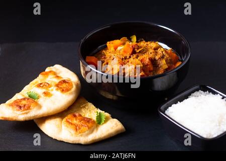 Orientalisches Speisekonzept würzig geerdete oder gehackte Köche masala Curry mit naanem Brot und Reis auf schwarzem Schieferhintergrund Stockfoto