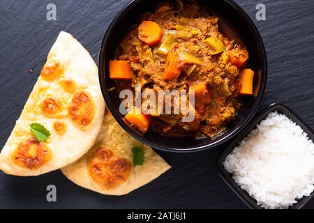 Orientalisches Speisekonzept würzig geerdete oder gehackte Köche masala Curry mit naanem Brot und Reis auf schwarzem Schieferhintergrund Stockfoto