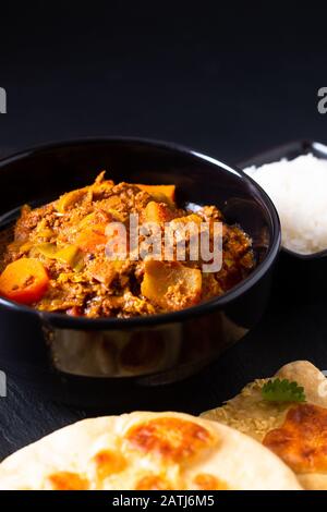 Orientalisches Speisekonzept würzig geerdete oder gehackte Köche masala Curry mit naanem Brot und Reis auf schwarzem Schieferhintergrund Stockfoto